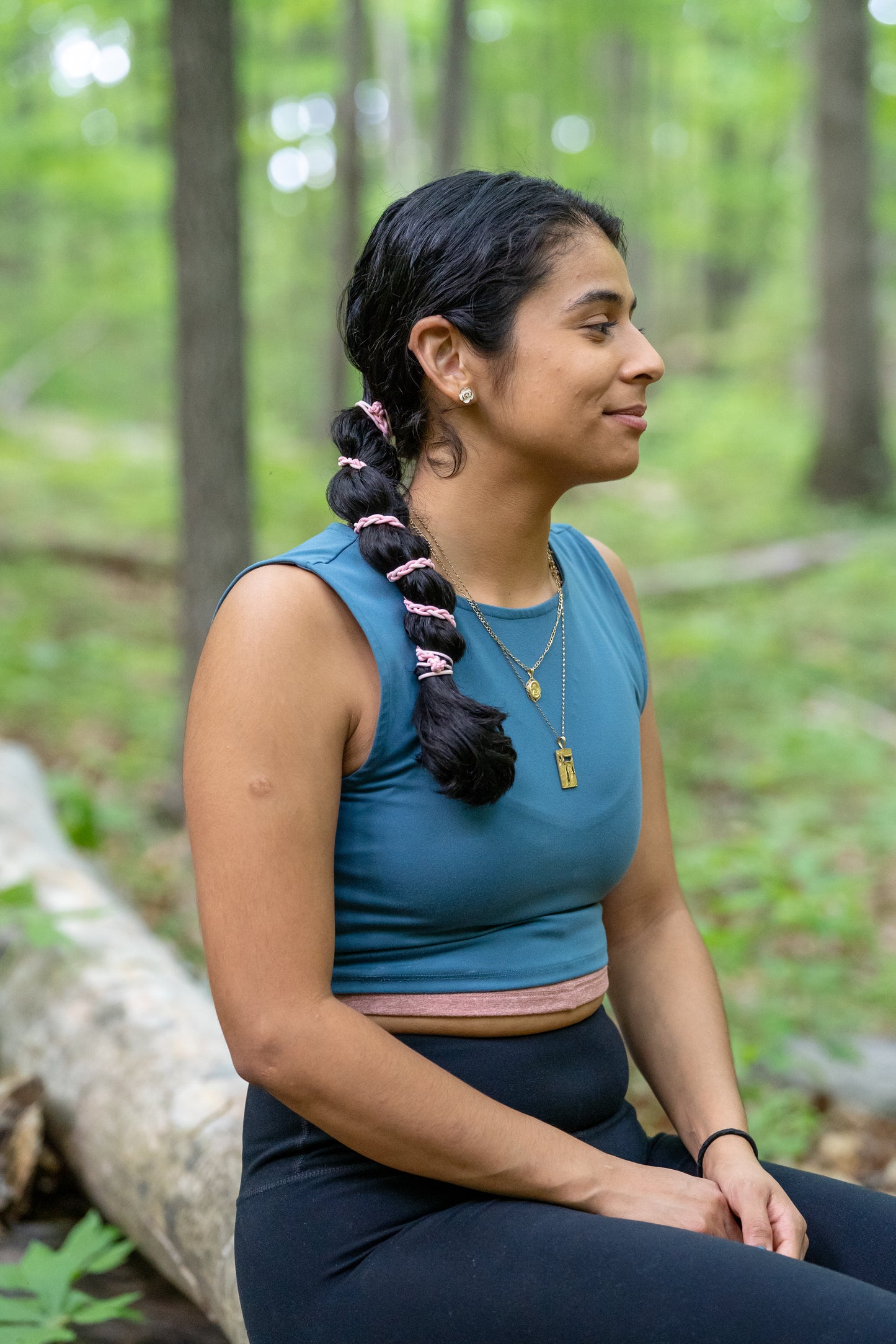 Girl with pink ponytail holder wrap around hair tie in thick curly hair in hiking clothes sitting in a forest