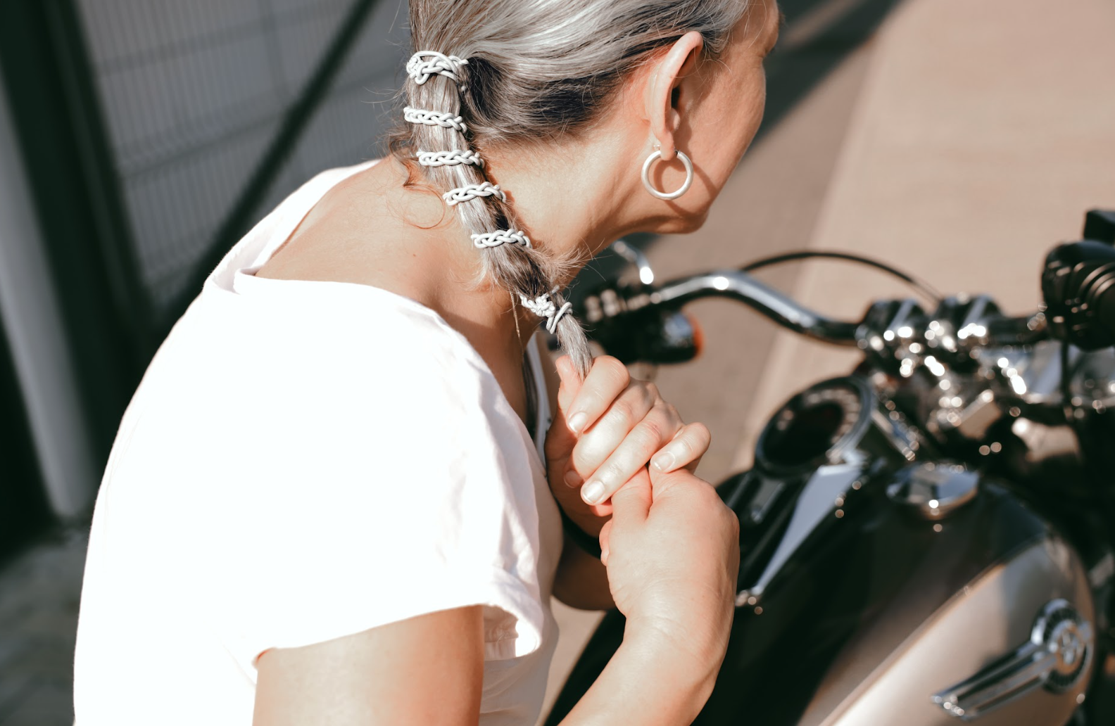 woman with motorcycle with grey hair and grey hair tie in her hair wrapped around her ponytail.