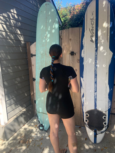 Woman with tangle free hairtie standing in front of two surfboards at the beach